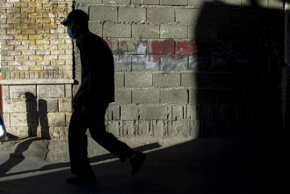 man in black hoodie walking on sidewalk during daytime