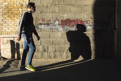 Woman in black joggers and white sneakers walking past a graffiti wall with yellow accents.
