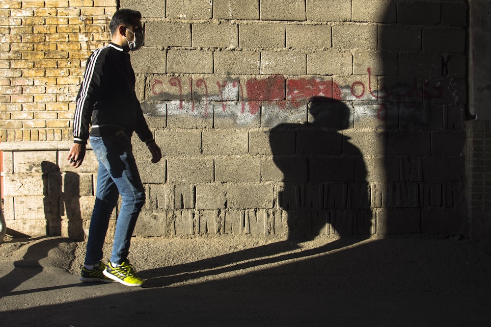 man in black jacket and blue denim jeans walking on sidewalk