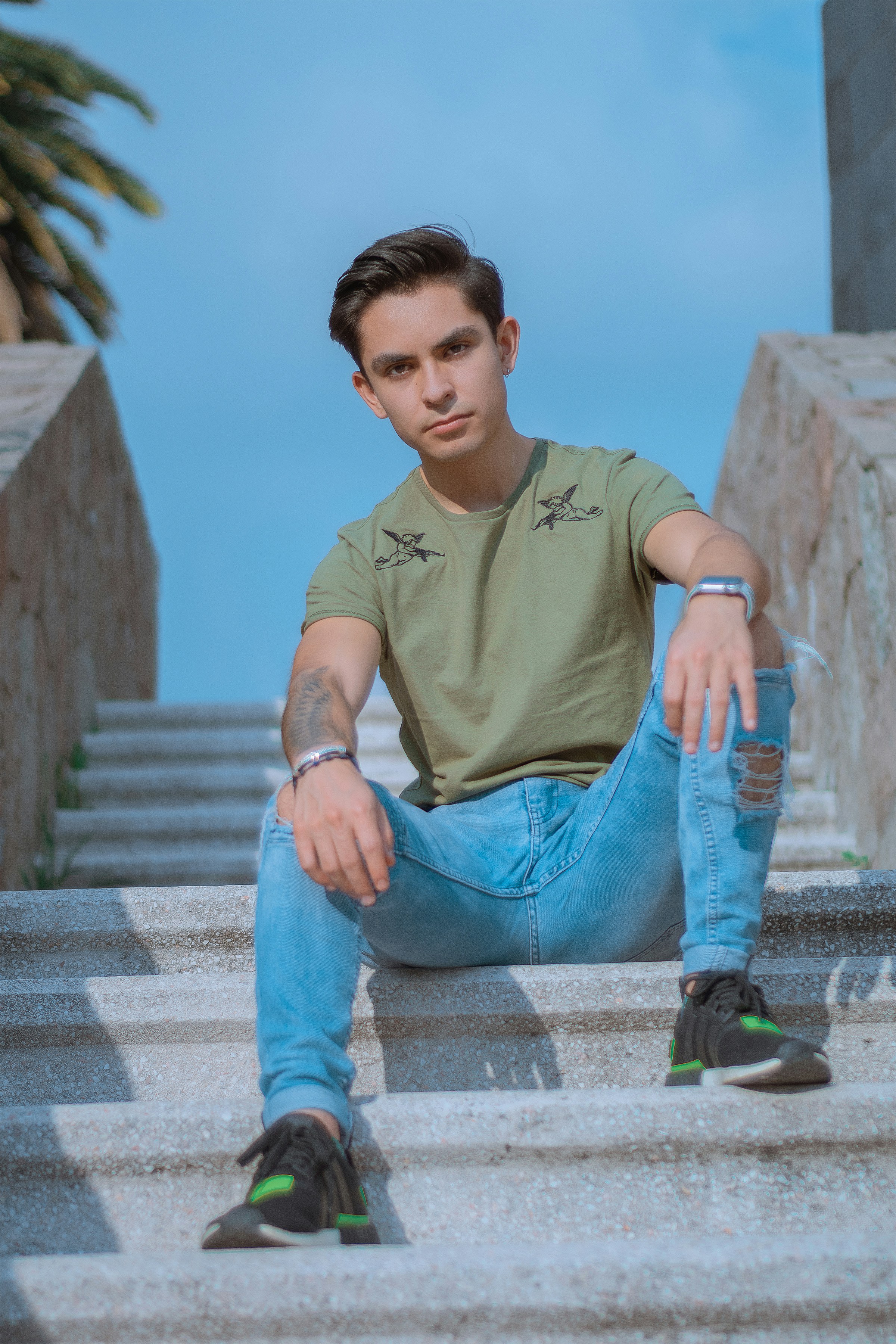 갈색 크루넥 티셔츠와 파란색 데님 청바지를 입은 남자가 콘크리트 계단에 앉아 있다.