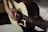 A person is playing an acoustic guitar, focusing on their hand positions. The musician is wearing a light-colored shirt. To the side, there is an open notebook with music notes and chord diagrams written on it.