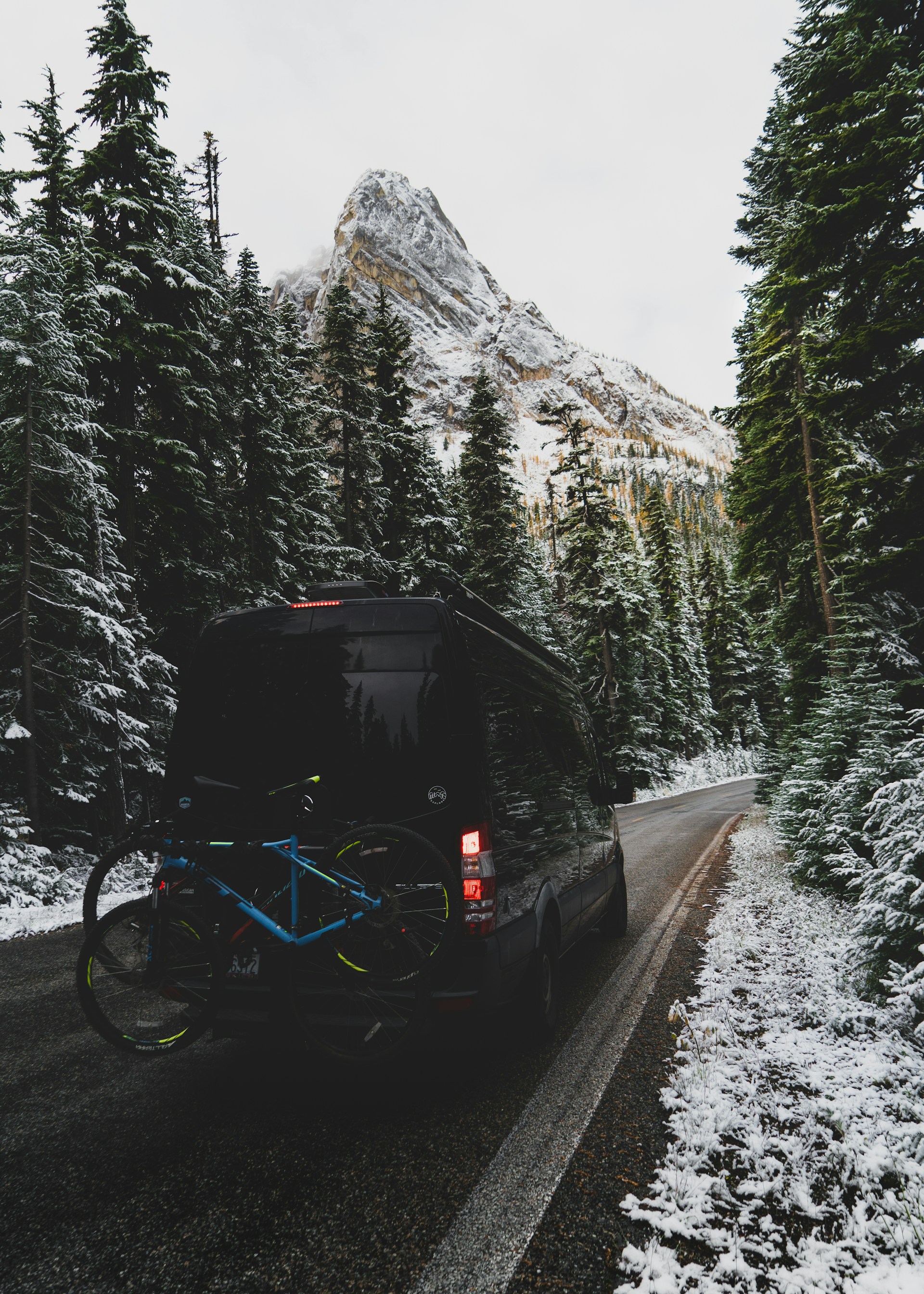 A robot delivering a parcel box on a snowy mountain trail surrounded by pine trees.