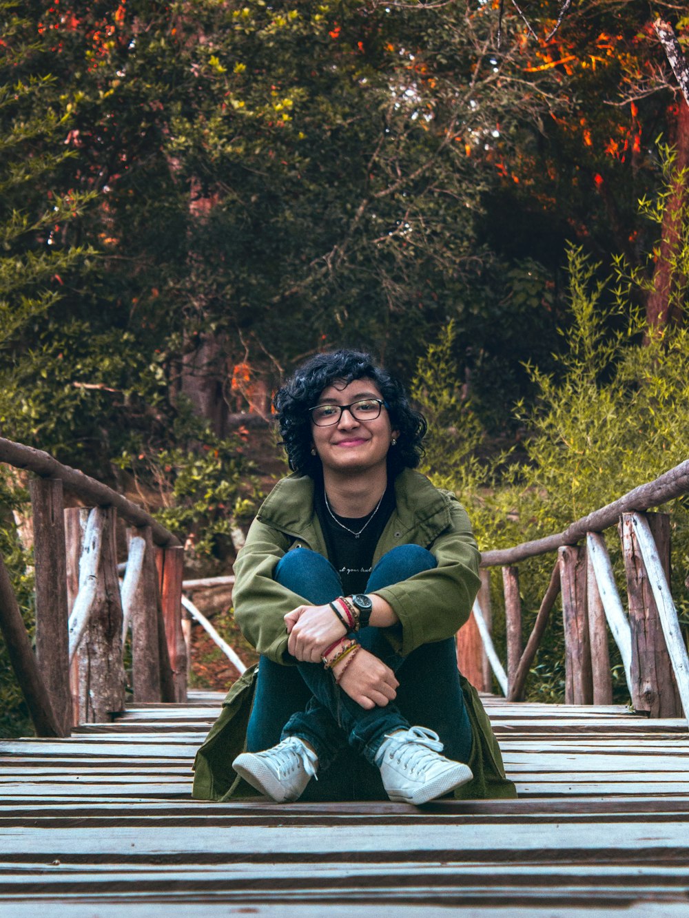 woman in green jacket sitting on wooden bridge