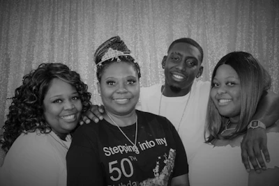 Friends laughing and wearing fun props like tiaras and feather boas in a photo booth with gold accents.