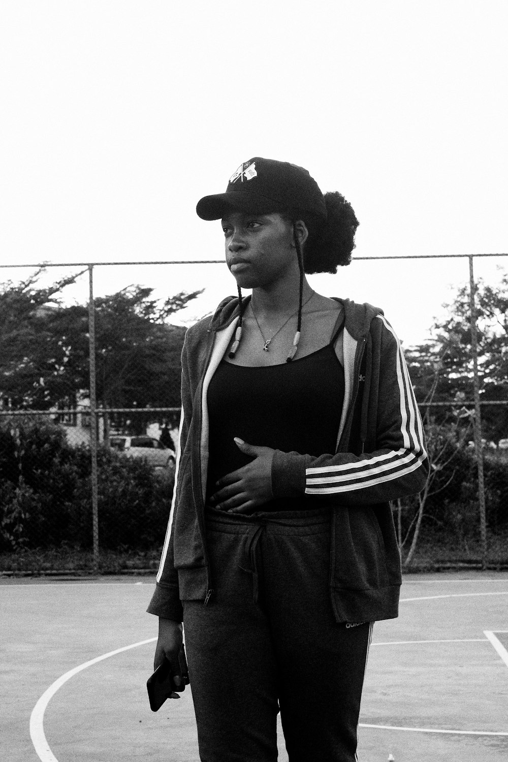 woman in black tank top and black hat standing on gray concrete pavement