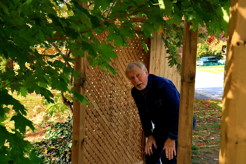 man in blue sweater standing near brown wooden fence