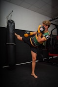 woman in green and black stripe tank top and black shorts carrying black and red boxing bag