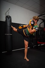 woman in green and black stripe tank top and black shorts carrying black and red boxing bag