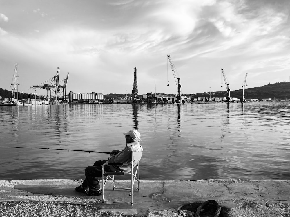 man sitting on chair near body of water