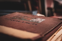 A close-up of an old book with a brown, slightly worn cover featuring the word 'ENGELSCH' in bold letters. The book has an ornate design with a blend of geometric and floral patterns near the top. The lighting is soft and creates a vintage atmosphere.