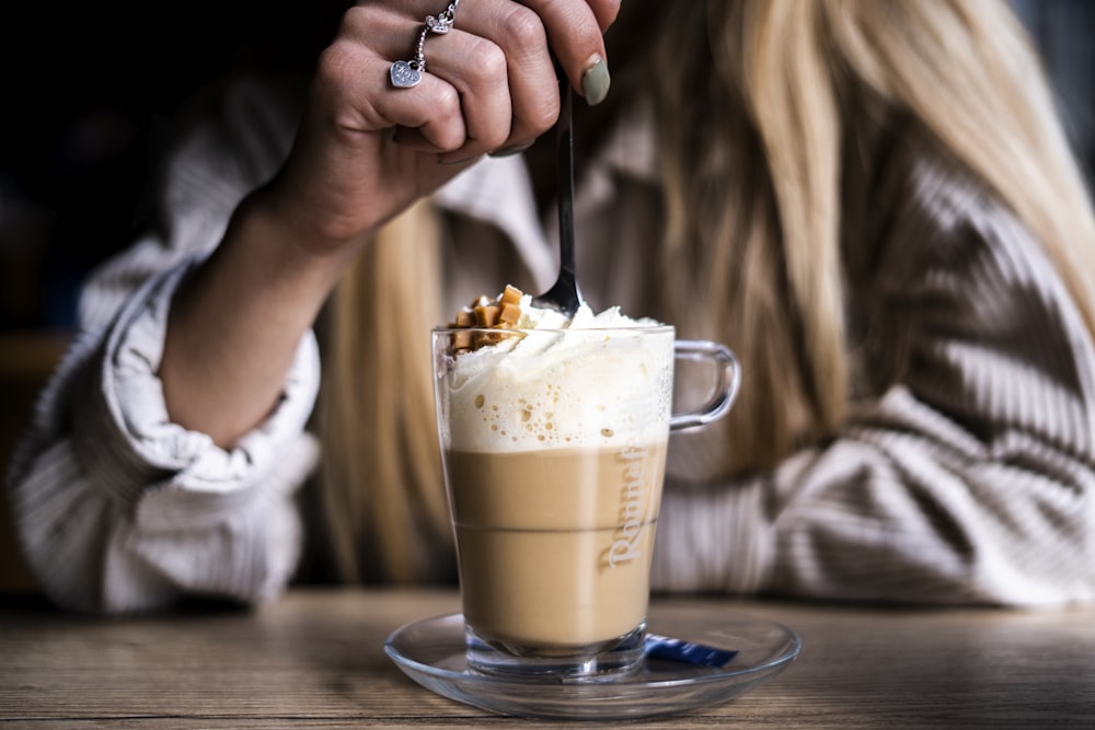 person holding clear glass mug with brown liquid