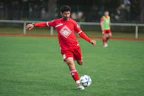 man in red soccer jersey kicking soccer ball on green grass field during daytime