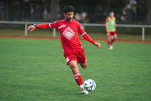 man in red soccer jersey kicking soccer ball on green grass field during daytime