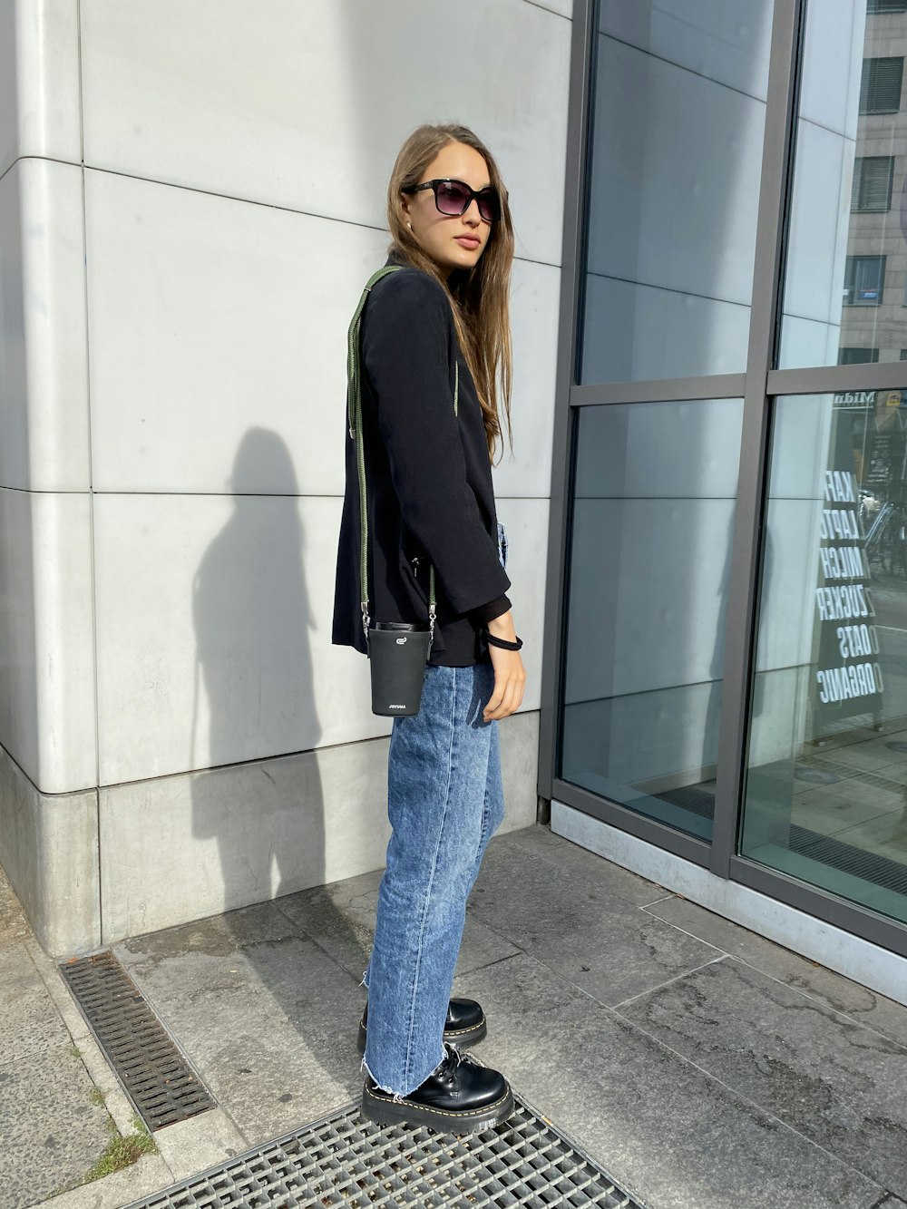 woman in black blazer and blue denim jeans standing near glass window