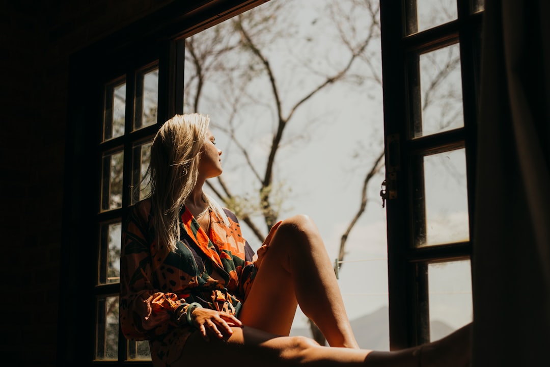 woman in red and white floral dress sitting on window during daytime