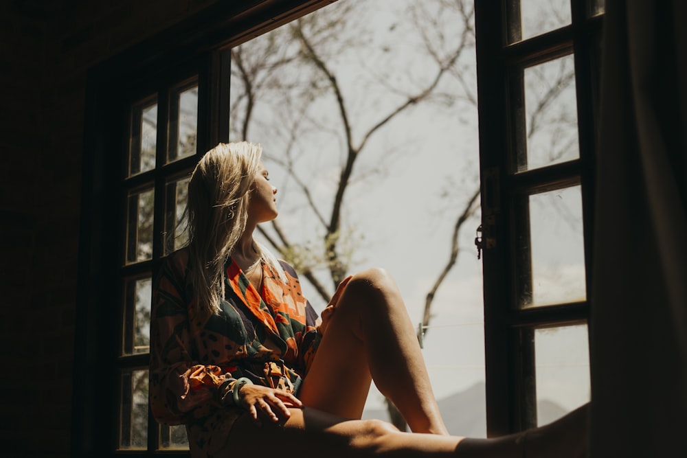 woman in red and white floral dress sitting on window during daytime