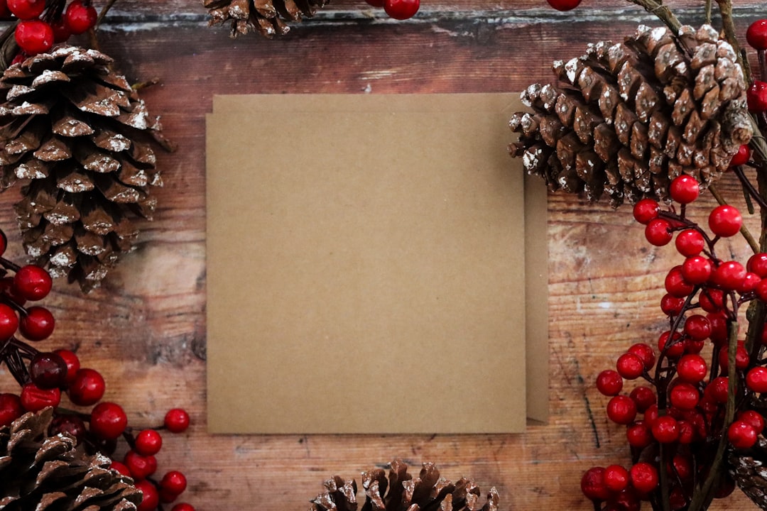 white paper on brown wooden table, Christmas Square Kraft Card with red berries and pine cones. Available here https://d