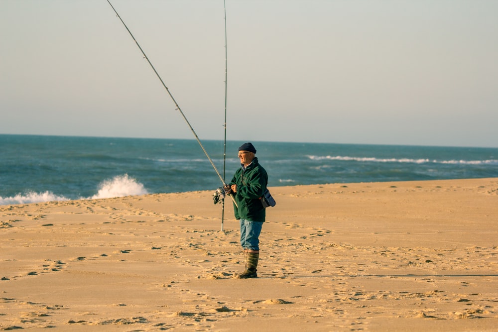 man in green jacket and brown pants fishing on beach during daytime