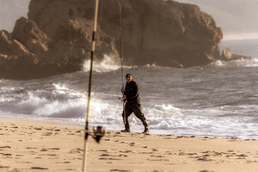 man in black jacket and pants standing on brown wooden stick on beach during daytime