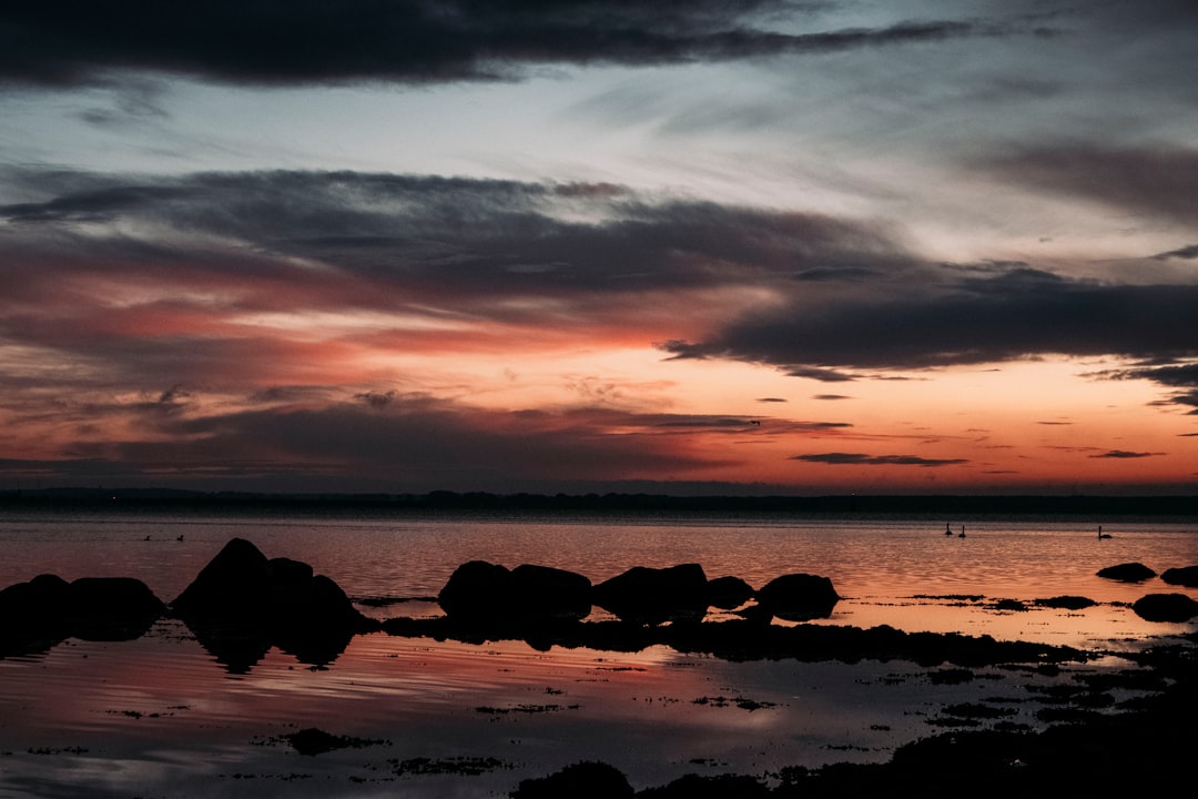 silhouette of rocks on sea shore during sunset