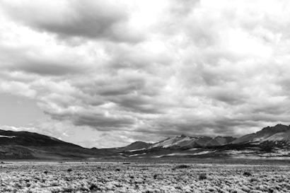 A vast, open landscape dominated by a grassy plain that stretches towards distant, rugged mountains under a dramatic, cloudy sky.