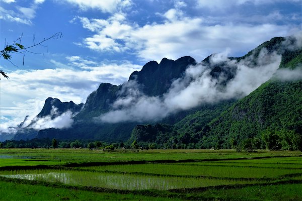 Green grass field near mountain under white clouds during daytime — Vang Vieng, Laos