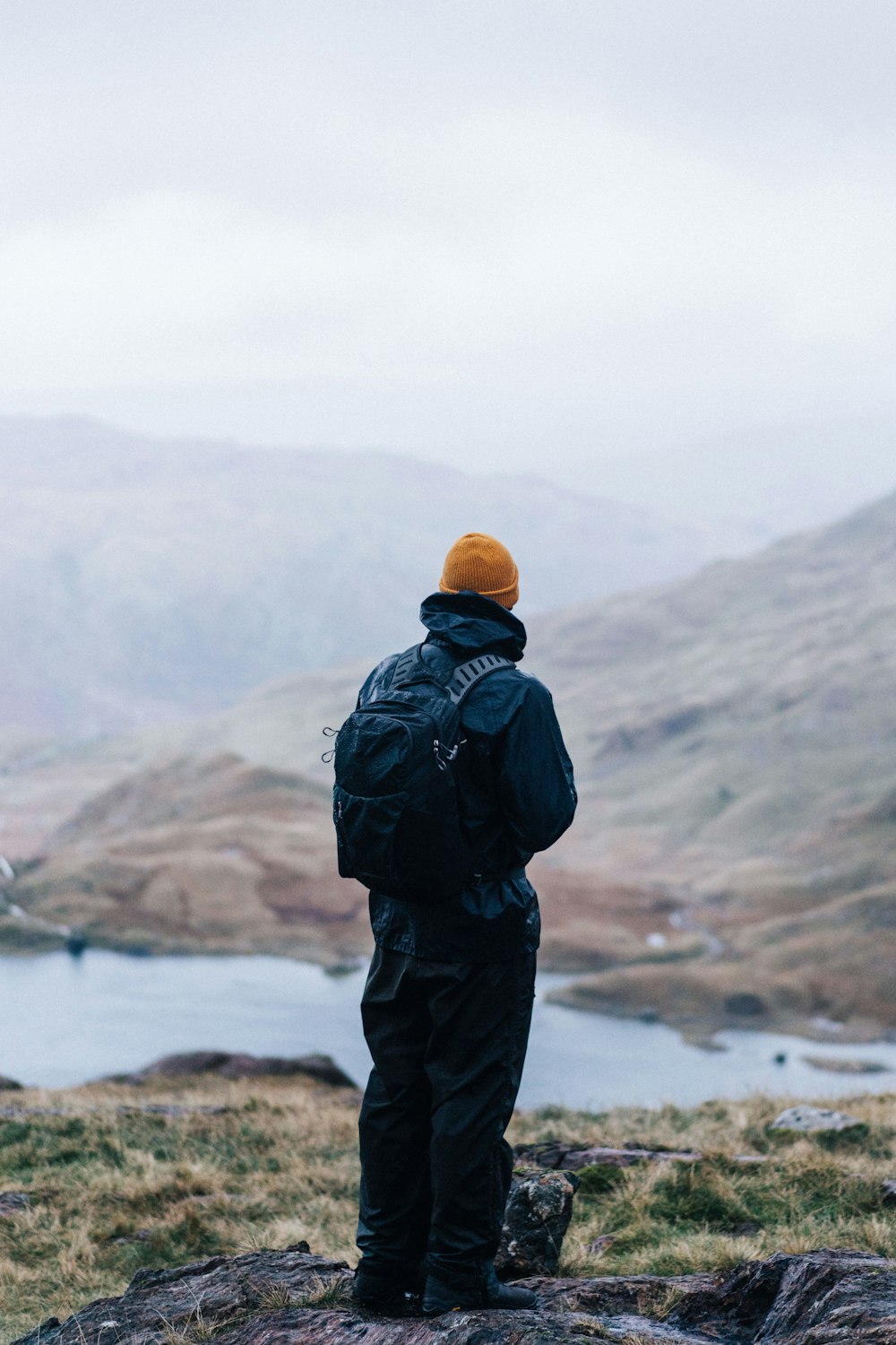 man in black jacket and brown knit cap standing on brown rock formation during daytime