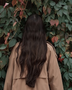 woman in brown coat standing near red flowers
