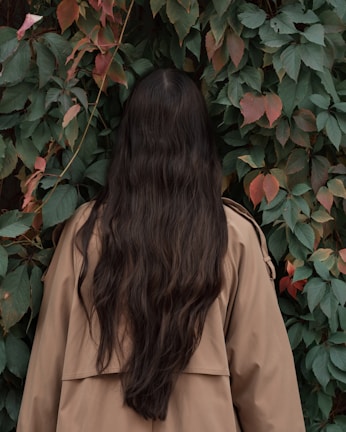 woman in brown coat standing near red flowers
