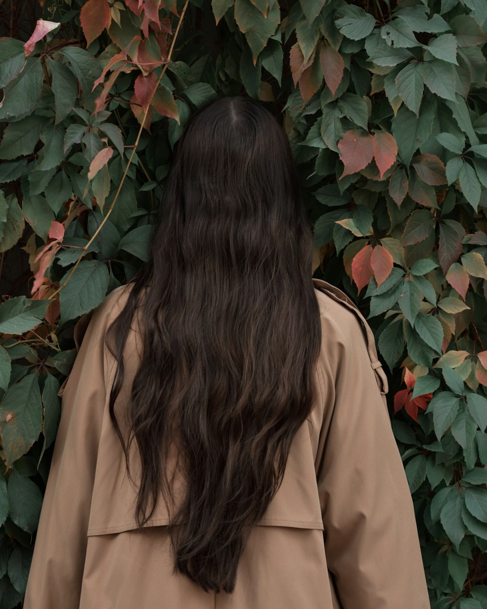 woman in brown coat standing near red flowers