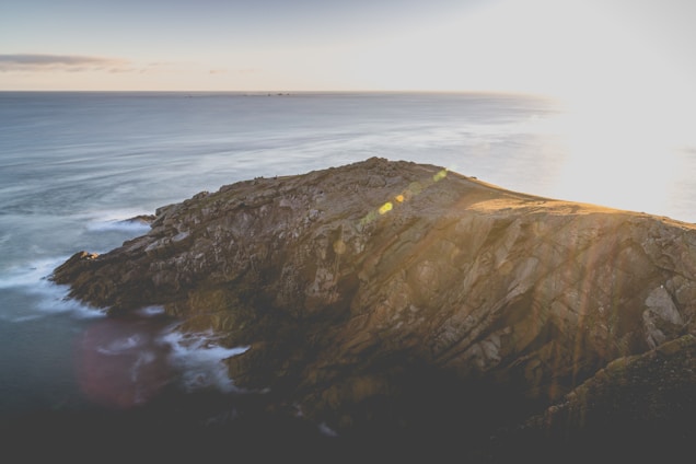A cinematic aerial shot of a rugged coastline at sunset, capturing the golden light and dramatic shadows.