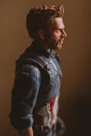 A detailed action figure of a bearded man wearing a blue suit with a red and white emblem. The figure is captured in profile against a neutral, softly lit background, highlighting the intricate design of the costume and the character's sculpted features.
