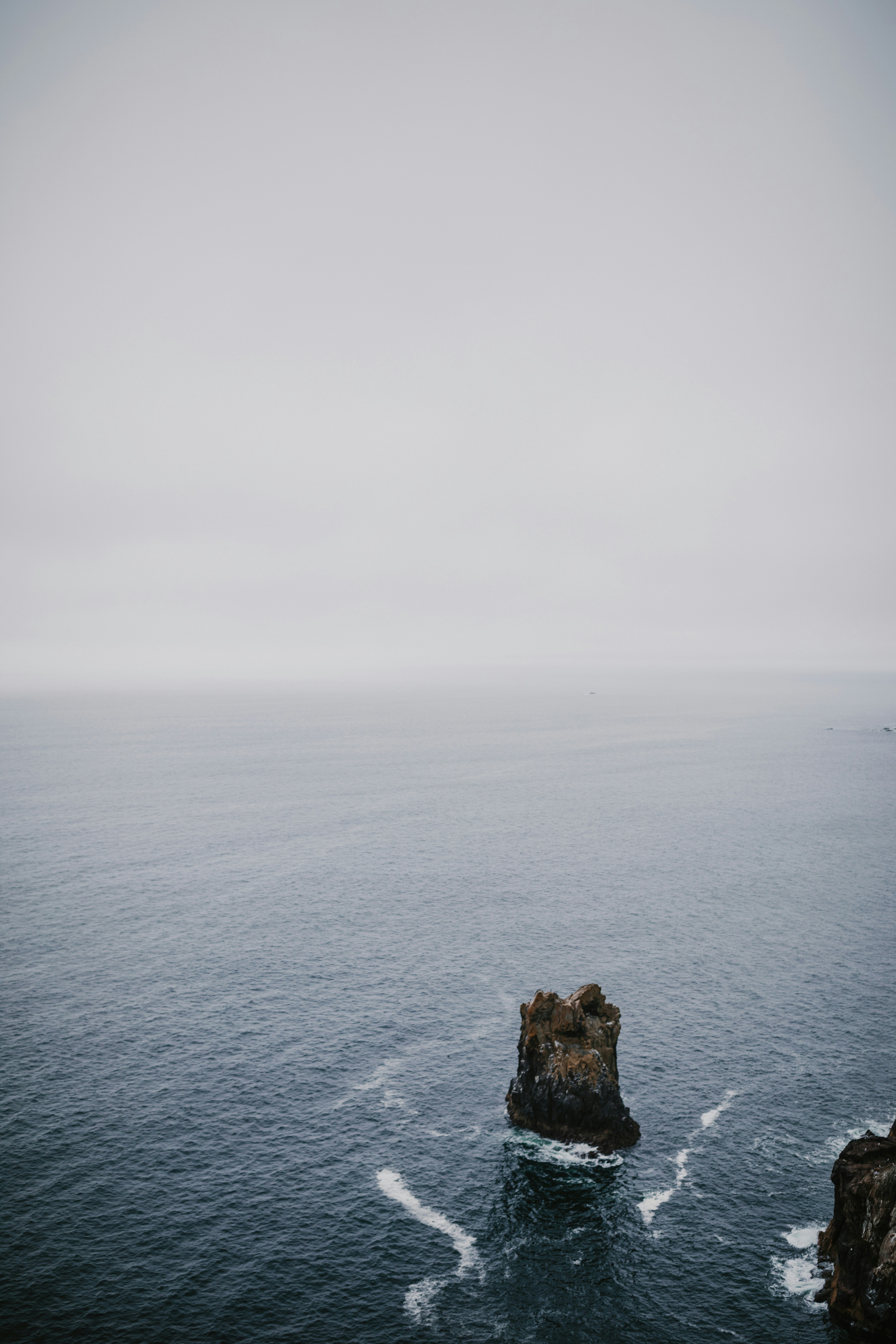 brown rock formation on sea under white sky during daytime