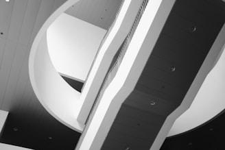 A modern architectural interior featuring large, sweeping curves and geometric patterns in a grayscale palette. The image captures a series of intersecting planes and staircases, with soft shadows and a smooth, minimalist design.