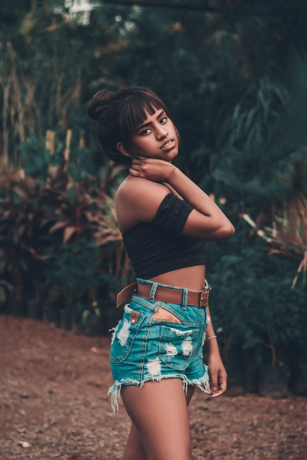 woman in black crop top and blue denim shorts standing on brown soil during daytime