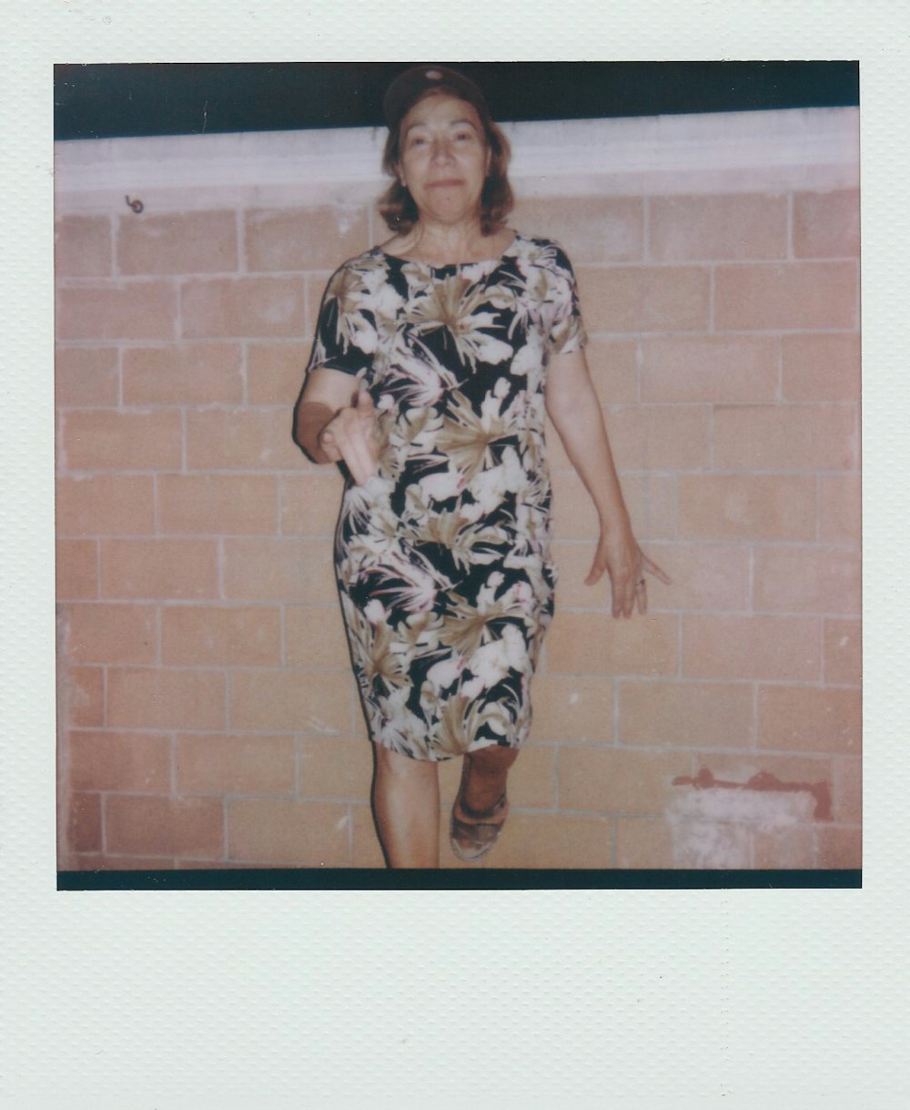 woman in black and white floral dress standing beside brown brick wall