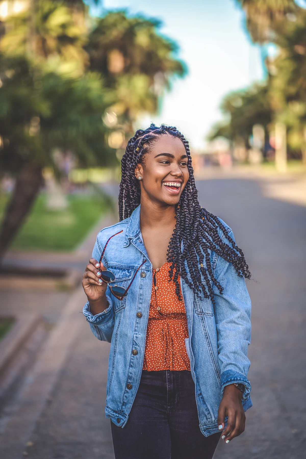 A smiling woman in a denim jacket walking down a city sidewalk