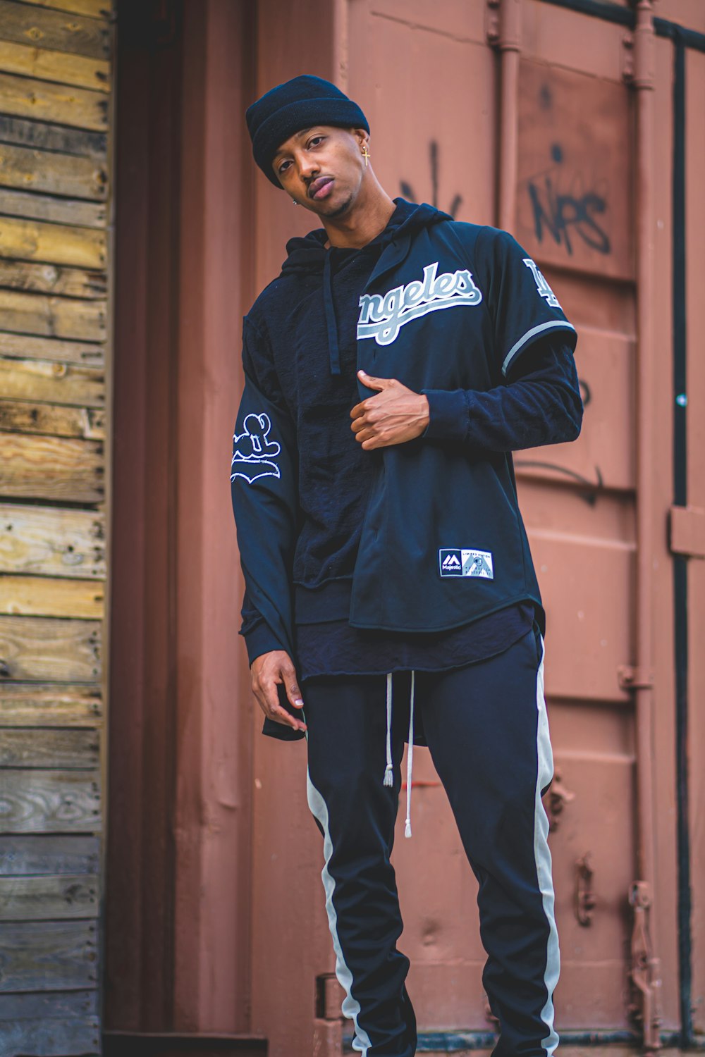 man in black and white adidas hoodie standing beside brown wooden wall