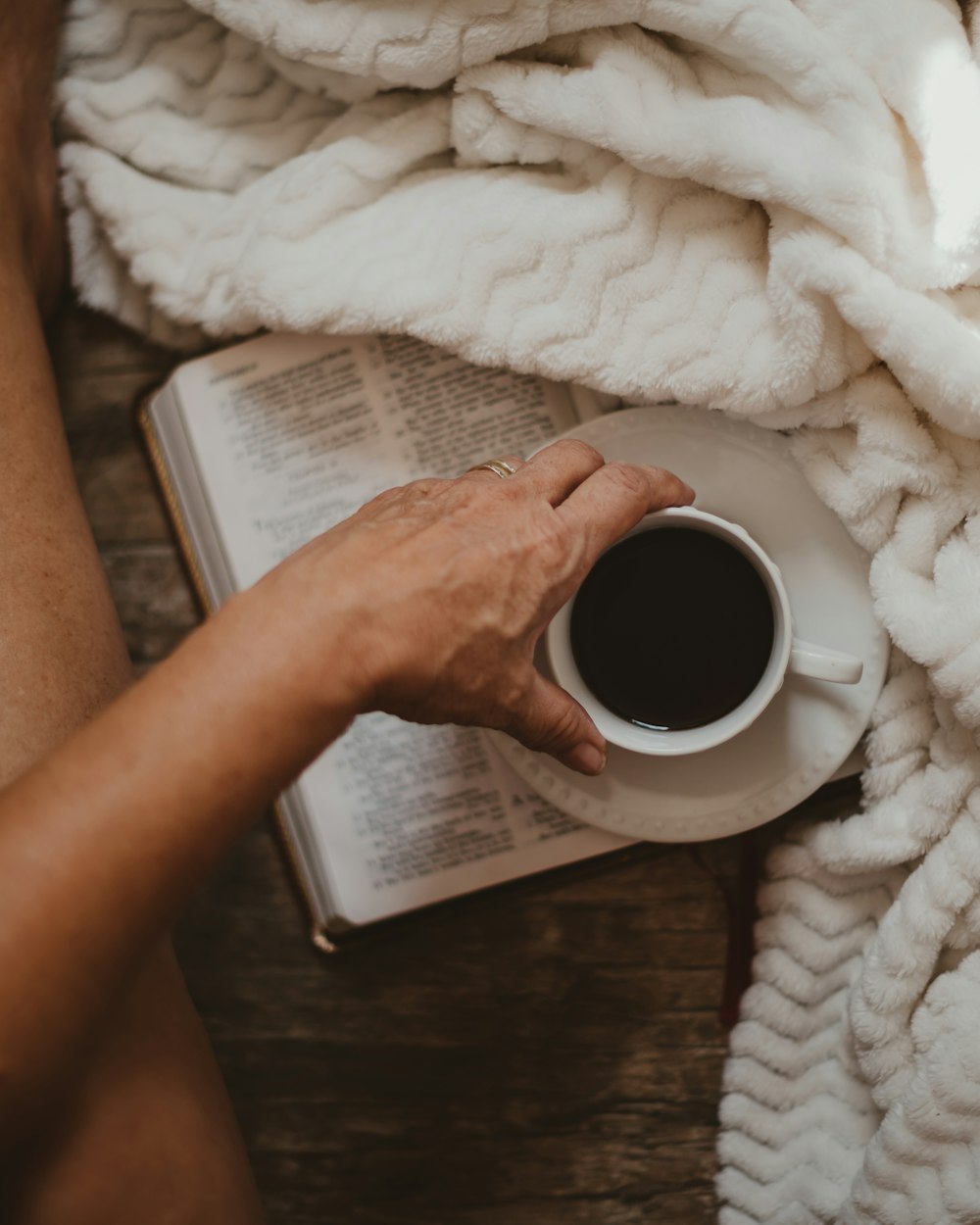 una persona leyendo un libro y sosteniendo una taza de café
