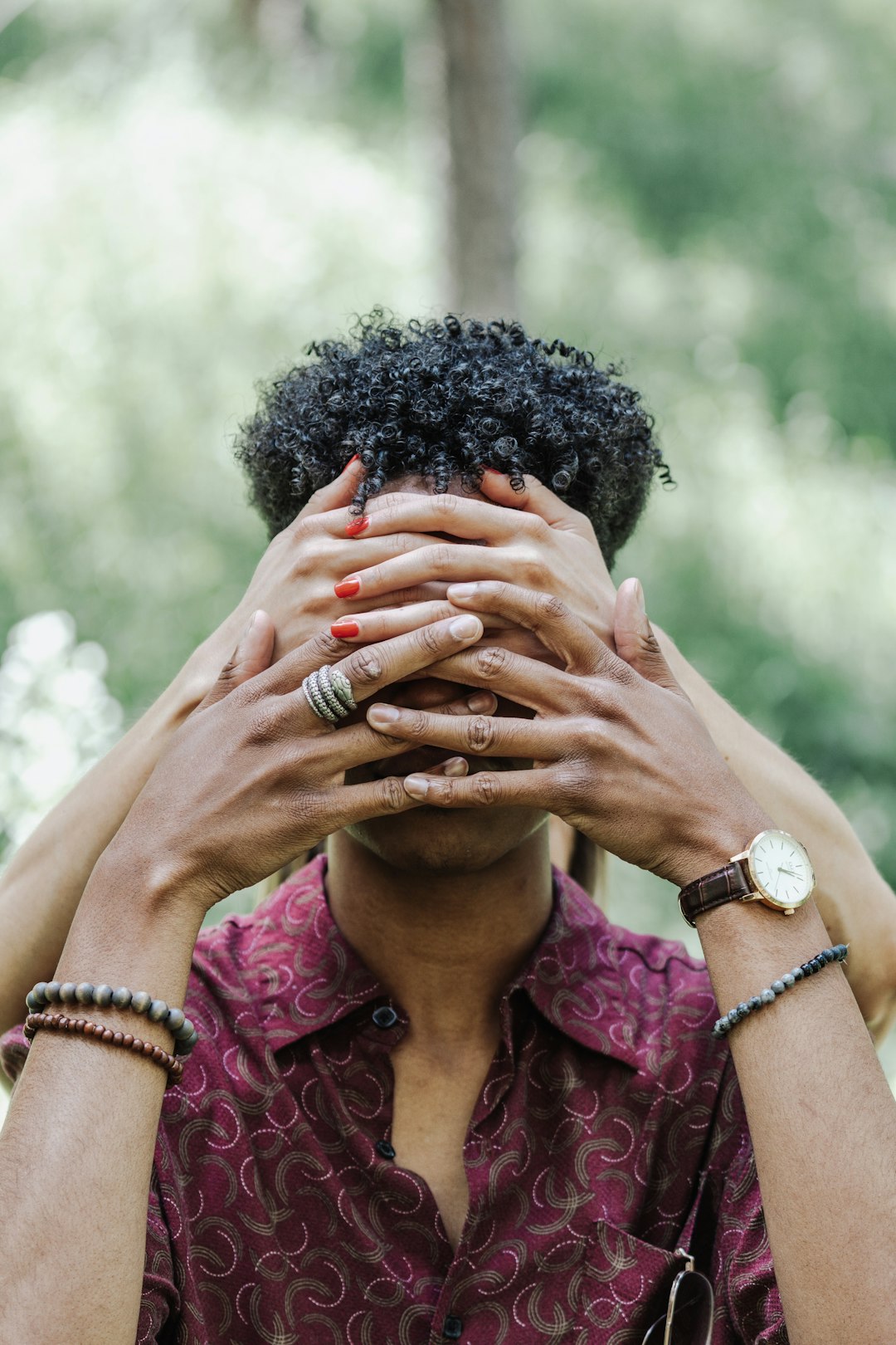 woman in pink and black floral shirt covering face with her hands