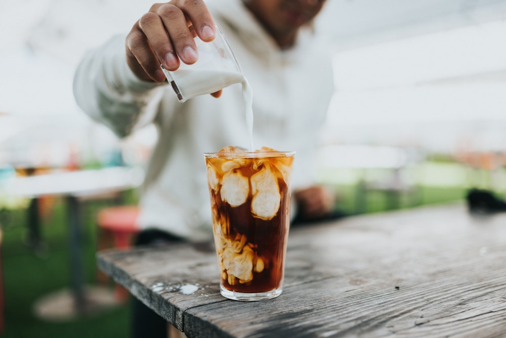 person holding clear drinking glass with brown liquid