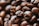 An up-close view of roasted coffee beans displaying their rich, dark brown texture and oily surface. The focus is on a cluster of beans with some slightly blurred in the background, emphasizing their natural, organic appearance.