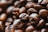 An up-close view of roasted coffee beans displaying their rich, dark brown texture and oily surface. The focus is on a cluster of beans with some slightly blurred in the background, emphasizing their natural, organic appearance.