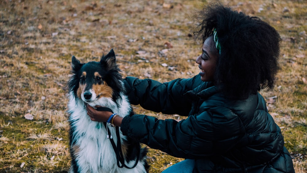 Donna in giacca verde che si siede accanto al cane a pelo lungo bianco nero e marrone durante il giorno