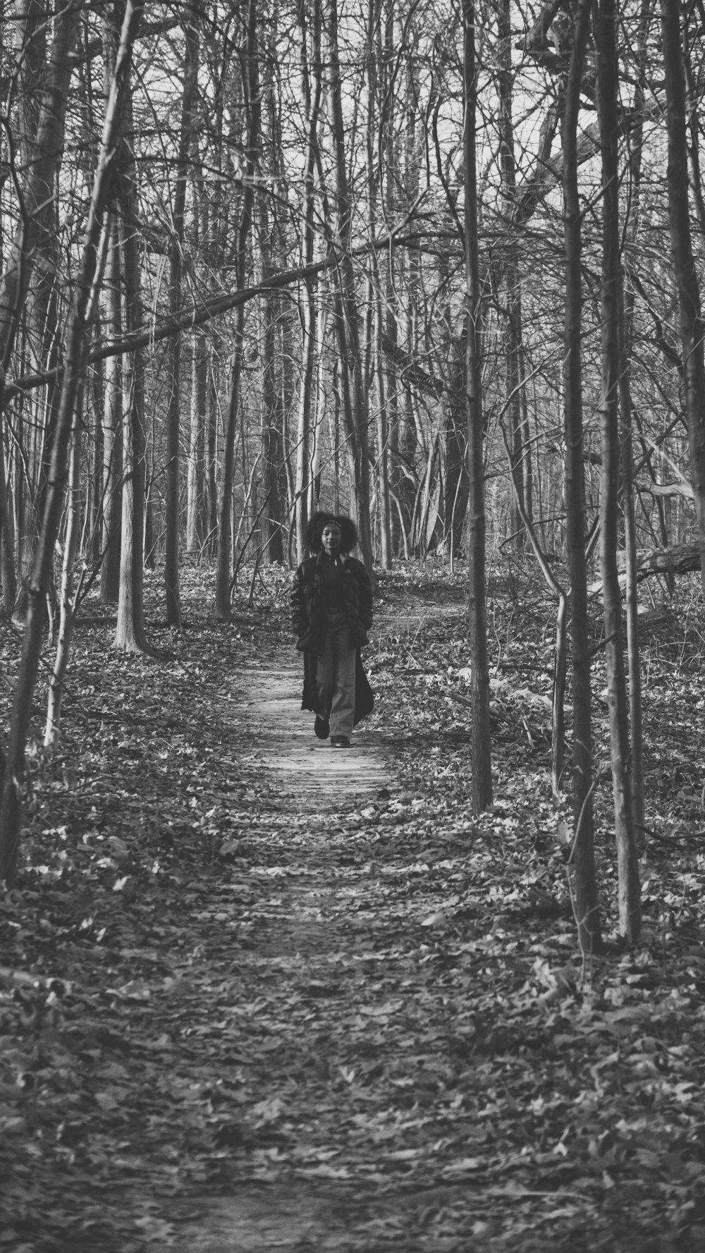 grayscale photo of woman in black coat walking on forest