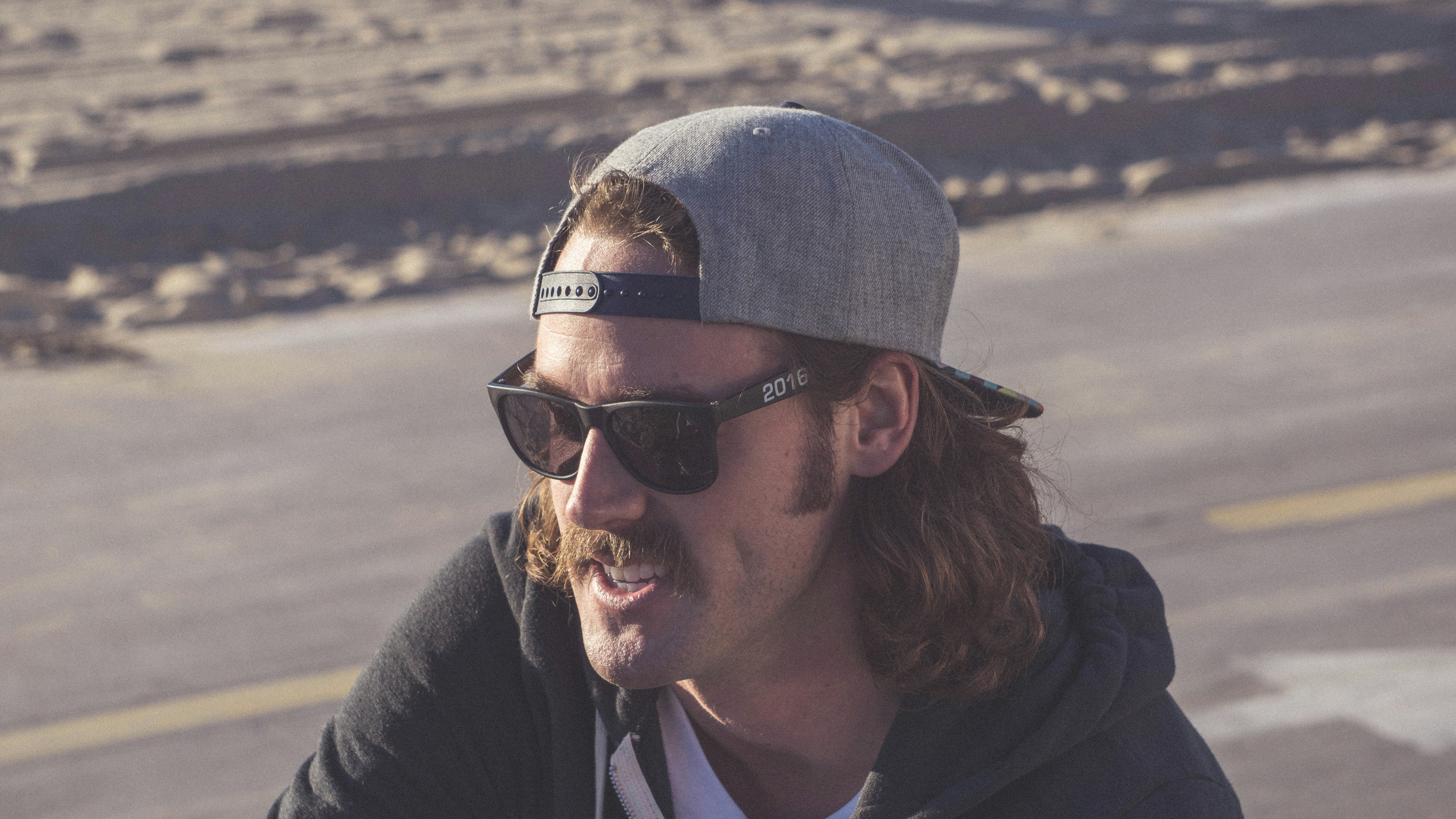 uomo in giacca nera che indossa berretto in maglia grigia e occhiali da sole neri