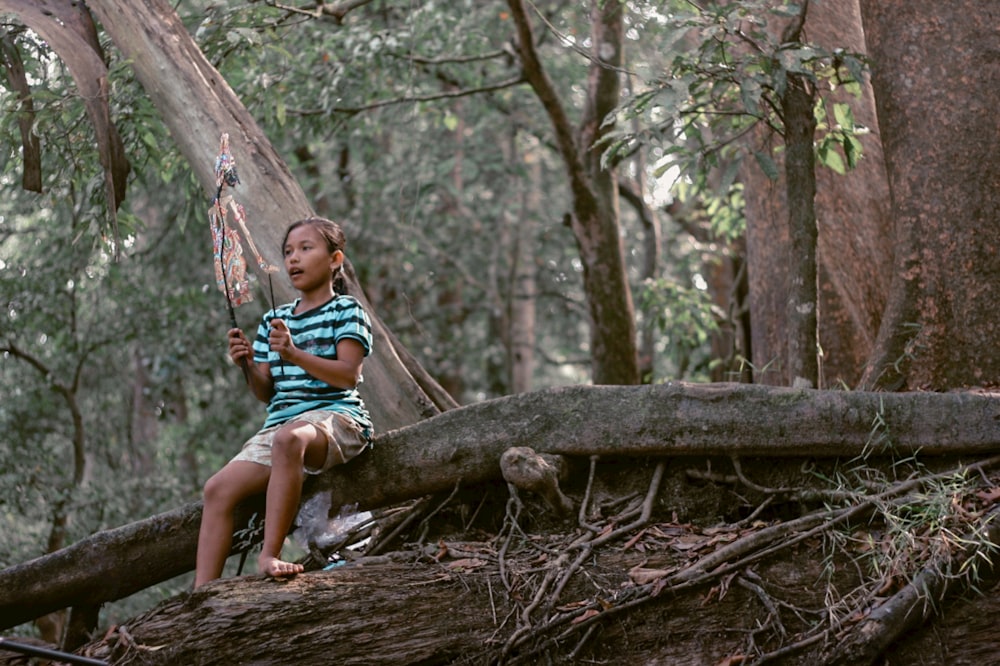 girl in blue and white stripe shirt sitting on brown tree log during daytime