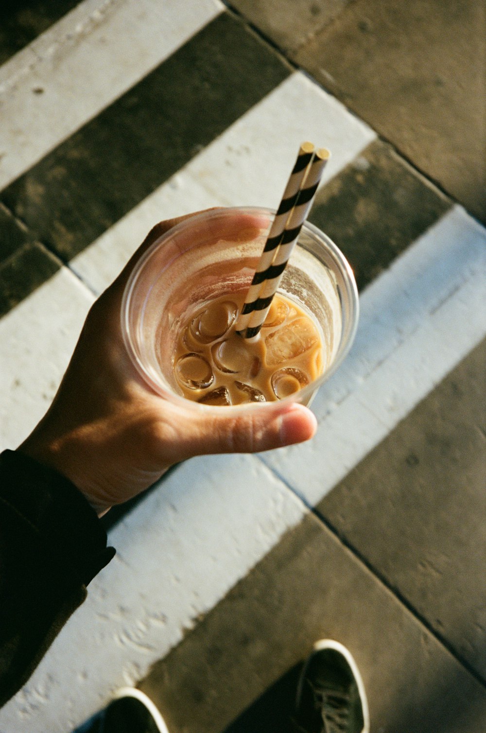 person holding clear plastic cup with brown liquid
