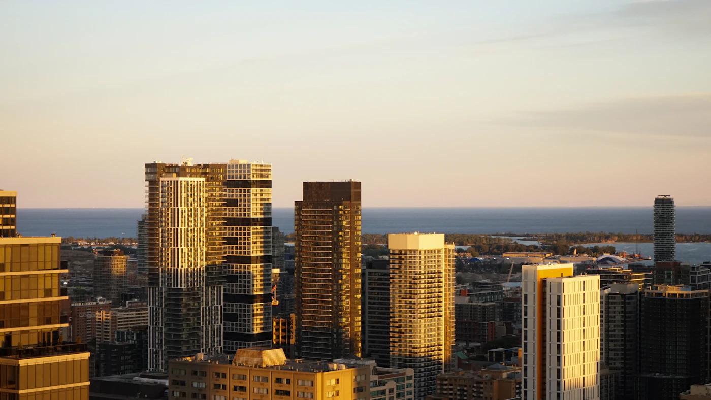 A cluster of Canadian downtown highrise towers glowing at golden hour with a lake on the horizon