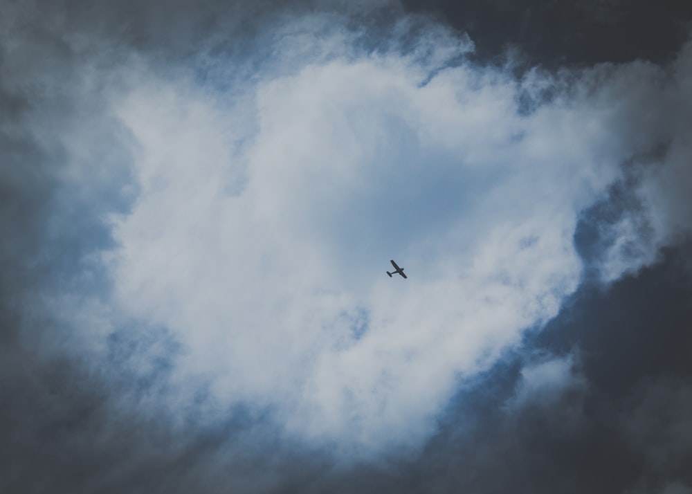 airplane flying under white clouds during daytime